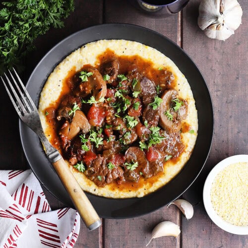 Bowl of grillades and grits garnished with chopped fresh parsley.