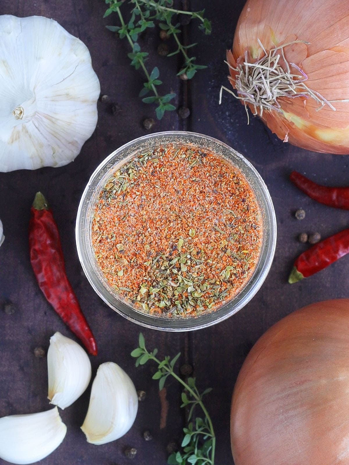 Homemade Cajun seasoning in a glass Mason jar with onions, garlic and seasonings in the background.