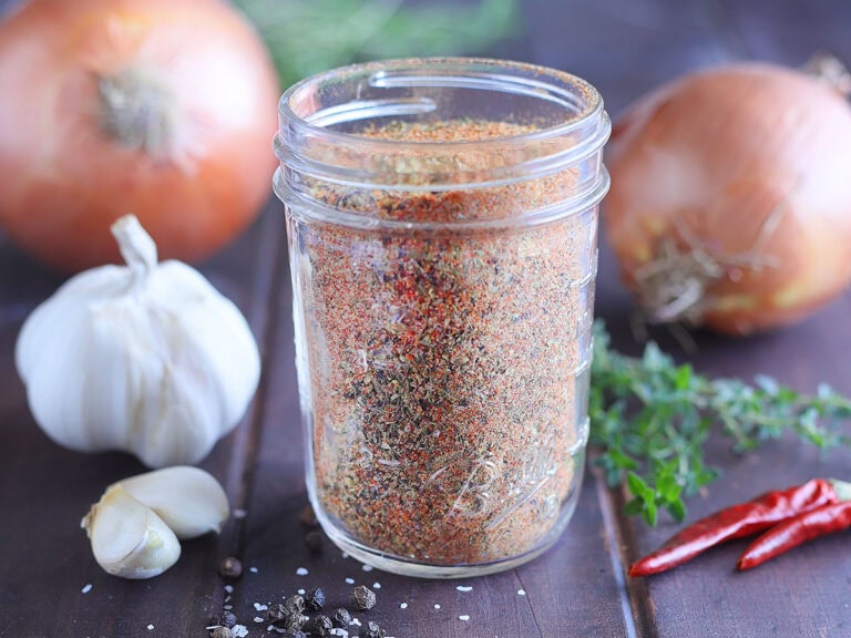 Homemade Cajun seasoning in a glass Mason jar with onions, garlic and seasonings in the background.