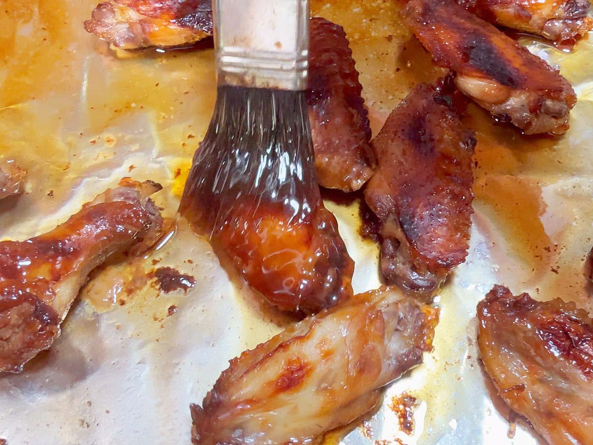 Brushing the reserved honey garlic sauce on cooked chicken wings.