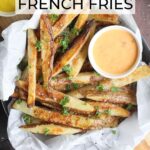 Oven baked French fries in a parchment paper lined dish garnished with salt and chopped fresh parsley.