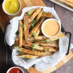 Oven baked French fries in a parchment paper lined dish garnished with salt and chopped fresh parsley.