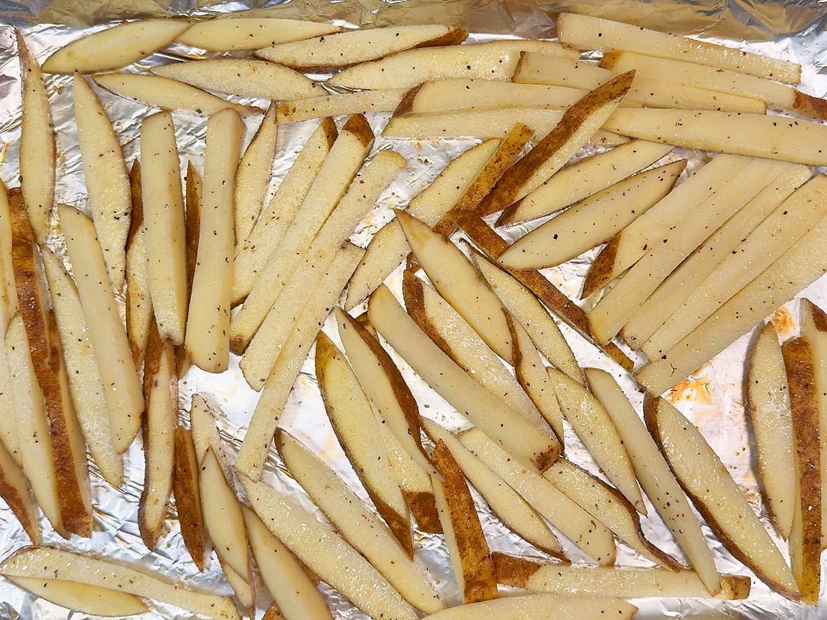 Seasoned cut potatoes on a foil lined and greased baking sheet.