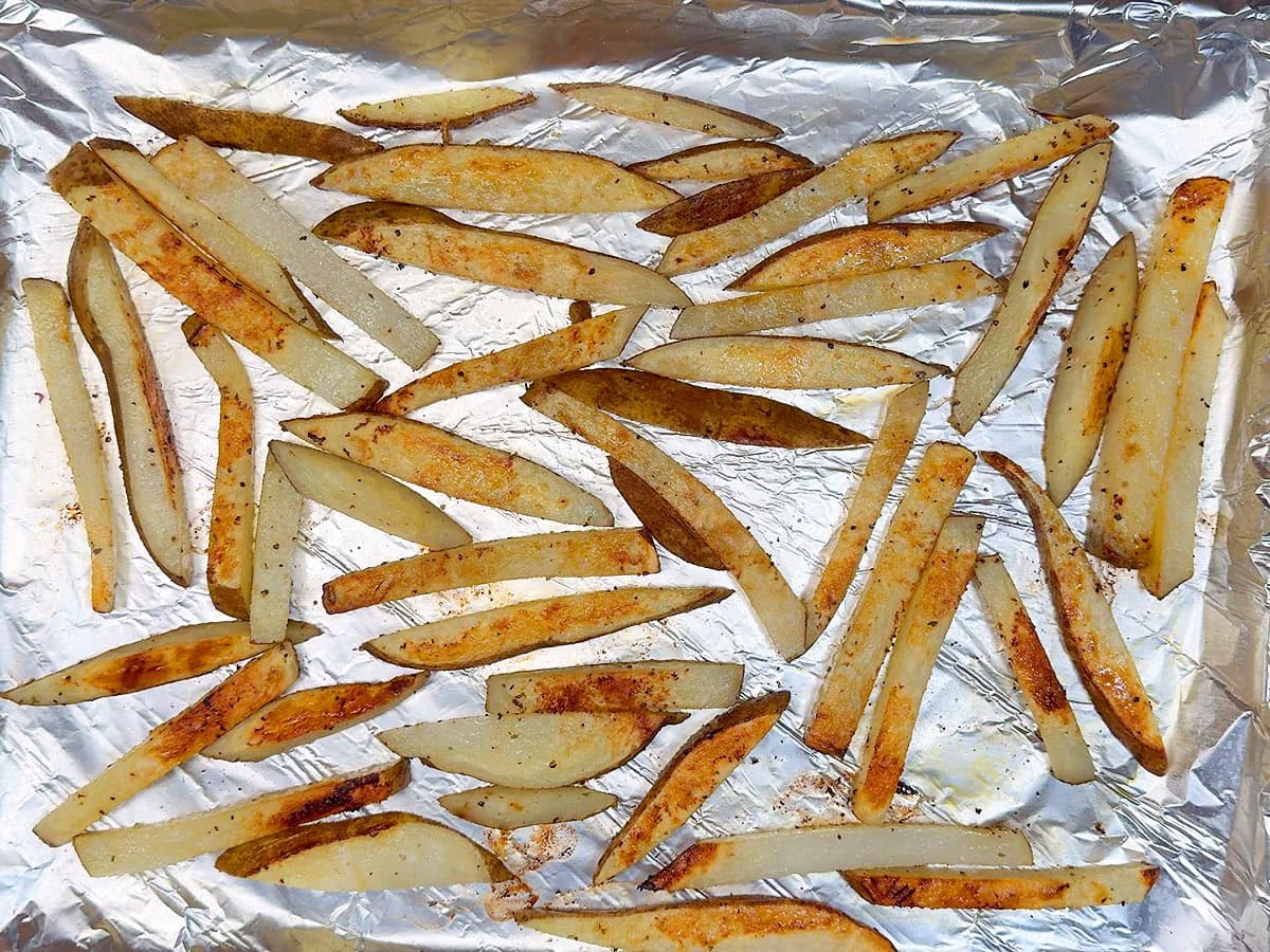Cooked oven baked French fries on a foiled lined and greased cookie sheet.