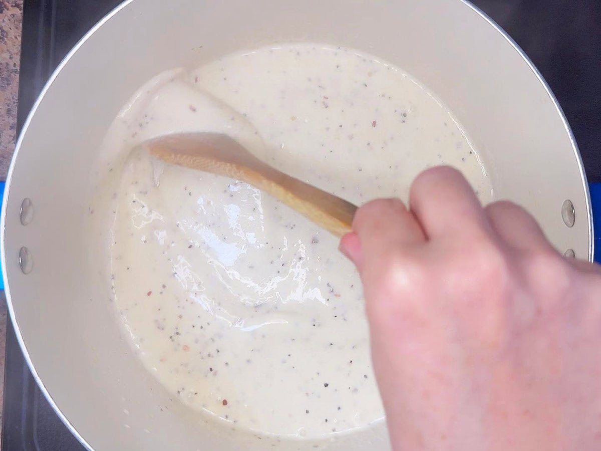 Stirring the alfredo sauce until the Parmesan cheese is melted.