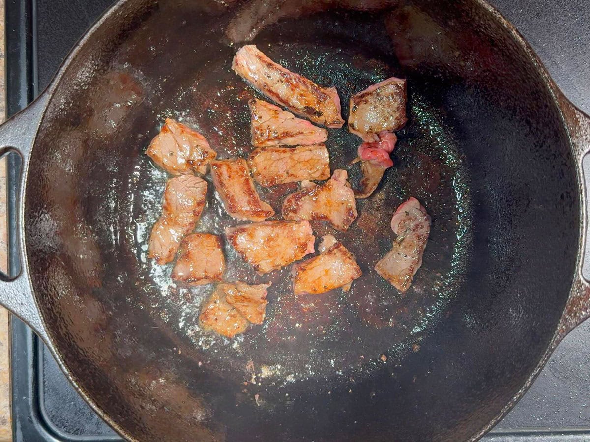 Pieces of browned round steak cooking in a cast iron Dutch oven.