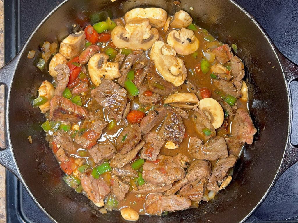 Browned round steak and sliced mushrooms added back into the Dutch oven with the sauteed vegetables, tomatoes and broth.