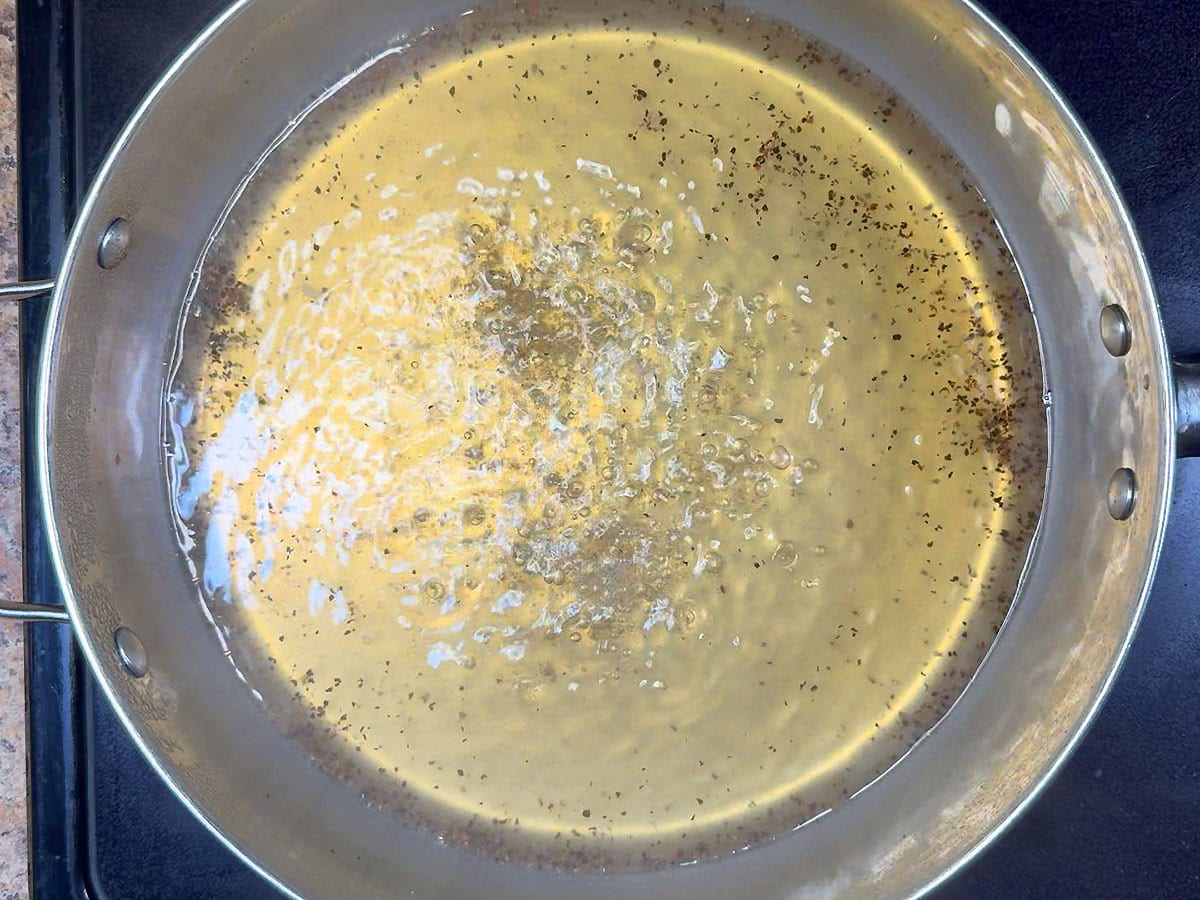 Chicken broth, water, salt, and black pepper simmering in a large saucepan.