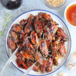 Large plate of honey garlic chicken wings garnished with fresh rosemary leaves.