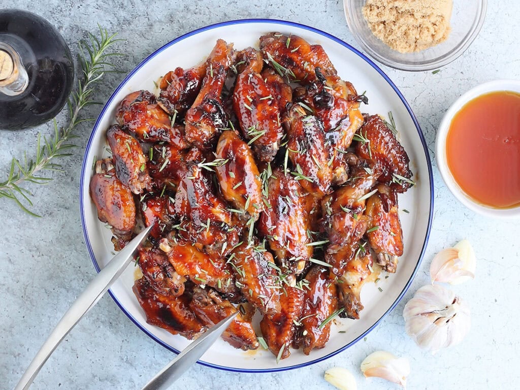 Large plate of honey garlic chicken wings garnished with fresh rosemary leaves.
