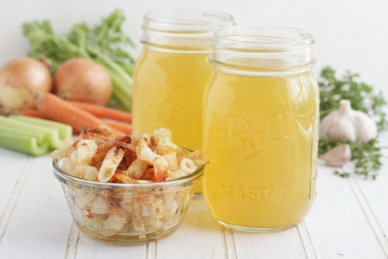 Two mason jars of shrimp stock with a small dish of shrimp shells and stock ingredients in the background.
