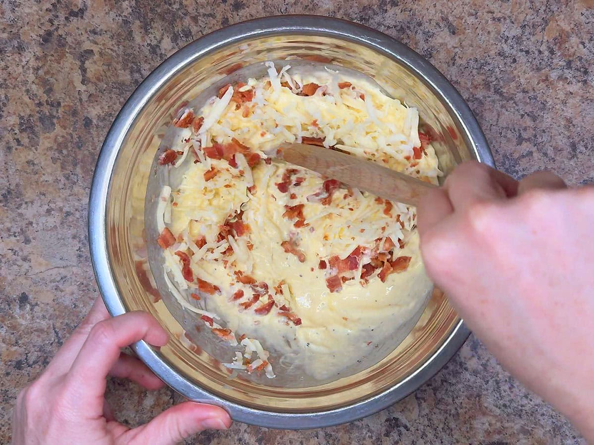 Mixing the pepper jack cheese and crumbled bacon into the egg mixture in a mixing bowl.