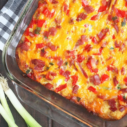 Baked breakfast ham casserole with tater tots on a wooden tabletop with three green onions on the side.