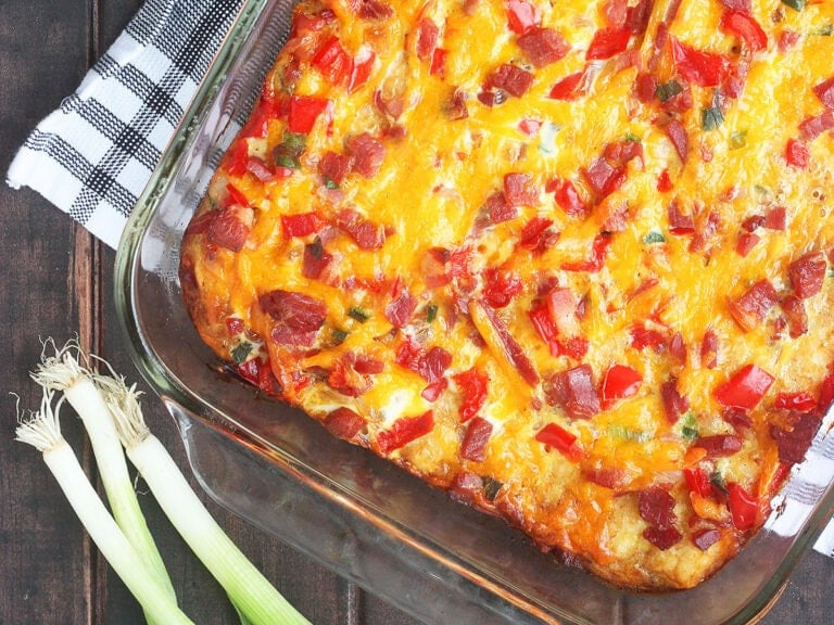 Baked breakfast ham casserole with tater tots on a wooden tabletop with three green onions on the side.