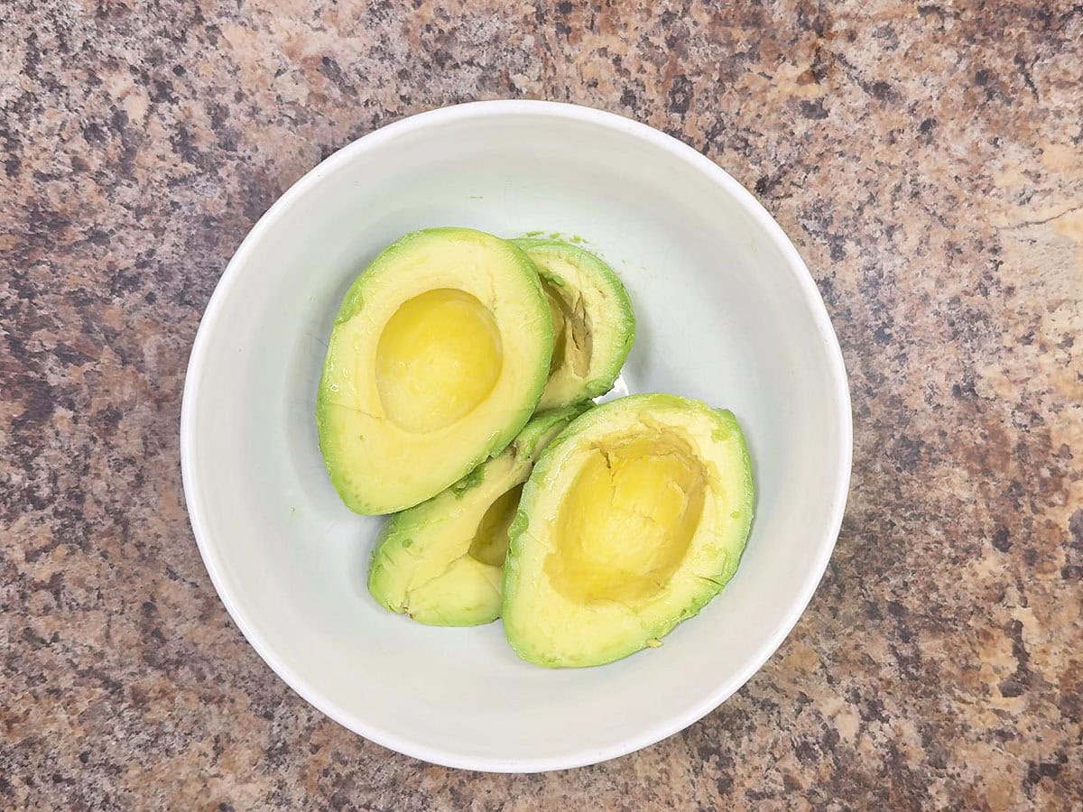 Halved and pitted avocados in a medium mixing bowl.