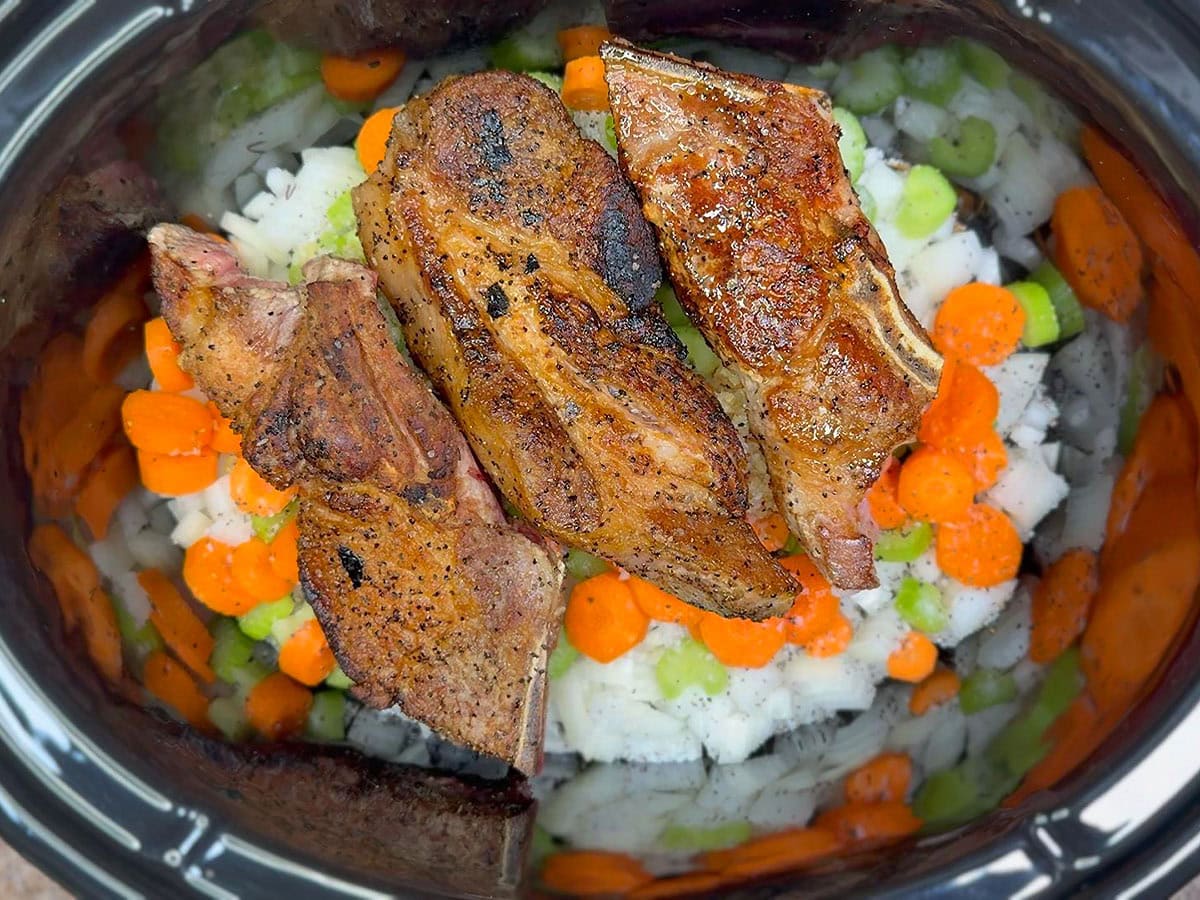 Browned country-style pork ribs nestled in the chopped vegetables in the crock of a slow cooker.