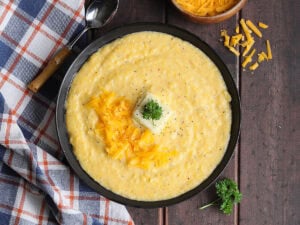 Bowl of cheese grits garnished with shredded cheese, a pat of butter, and a sprig of parsley.