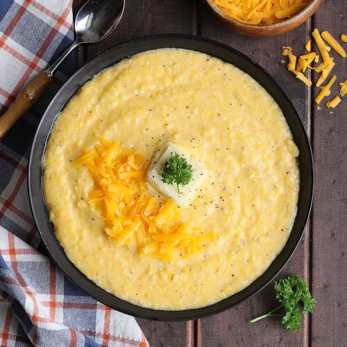 Bowl of cheese grits garnished with shredded cheese, a pat of butter, and a sprig of parsley.