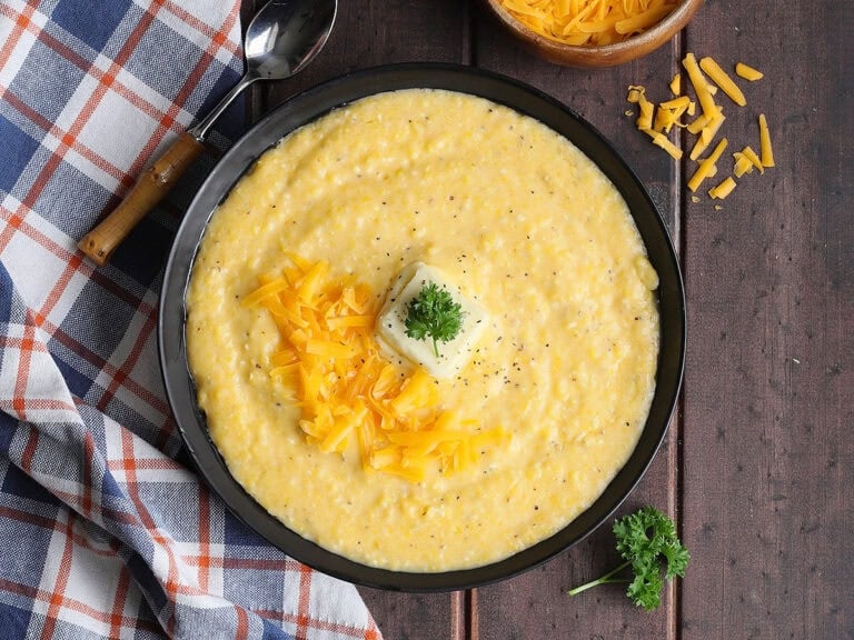 Bowl of cheese grits garnished with shredded cheese, a pat of butter, and a sprig of parsley.