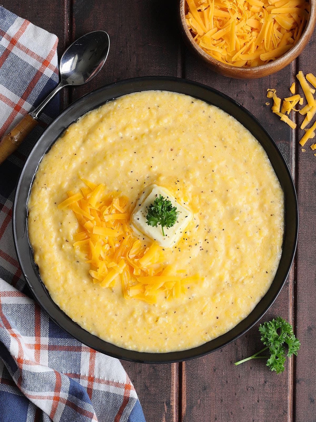 Bowl of cheese grits garnished with shredded cheese, a pat of butter, and a sprig of parsley.