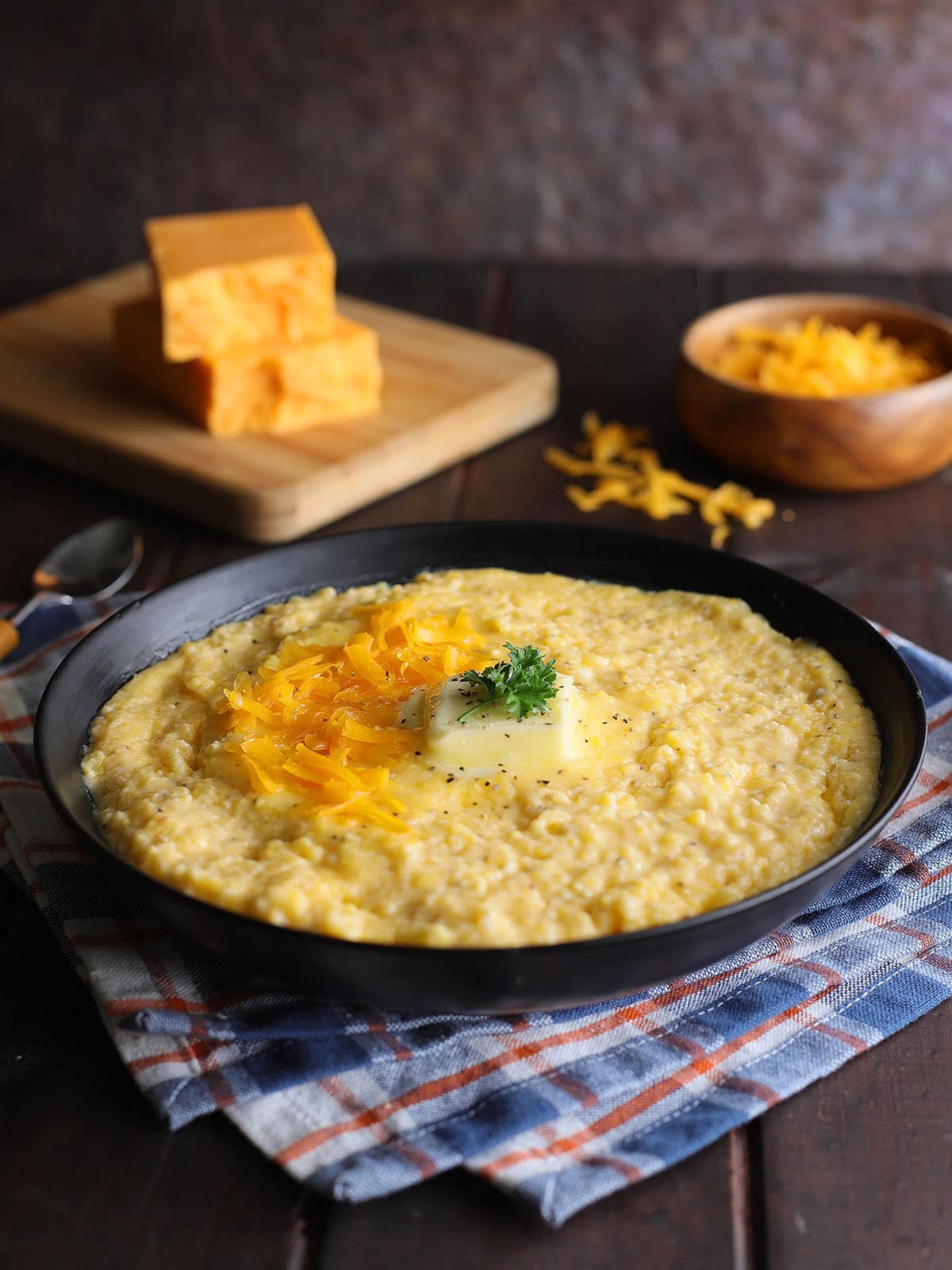 Bowl of cheese grits garnished with shredded cheese, a pat of butter, and a sprig of parsley.