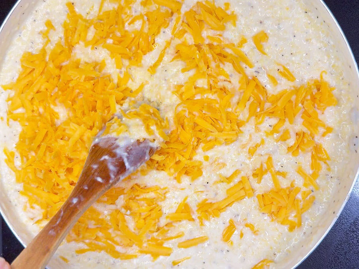 Stirring the shredded cheese into the cooked grits.