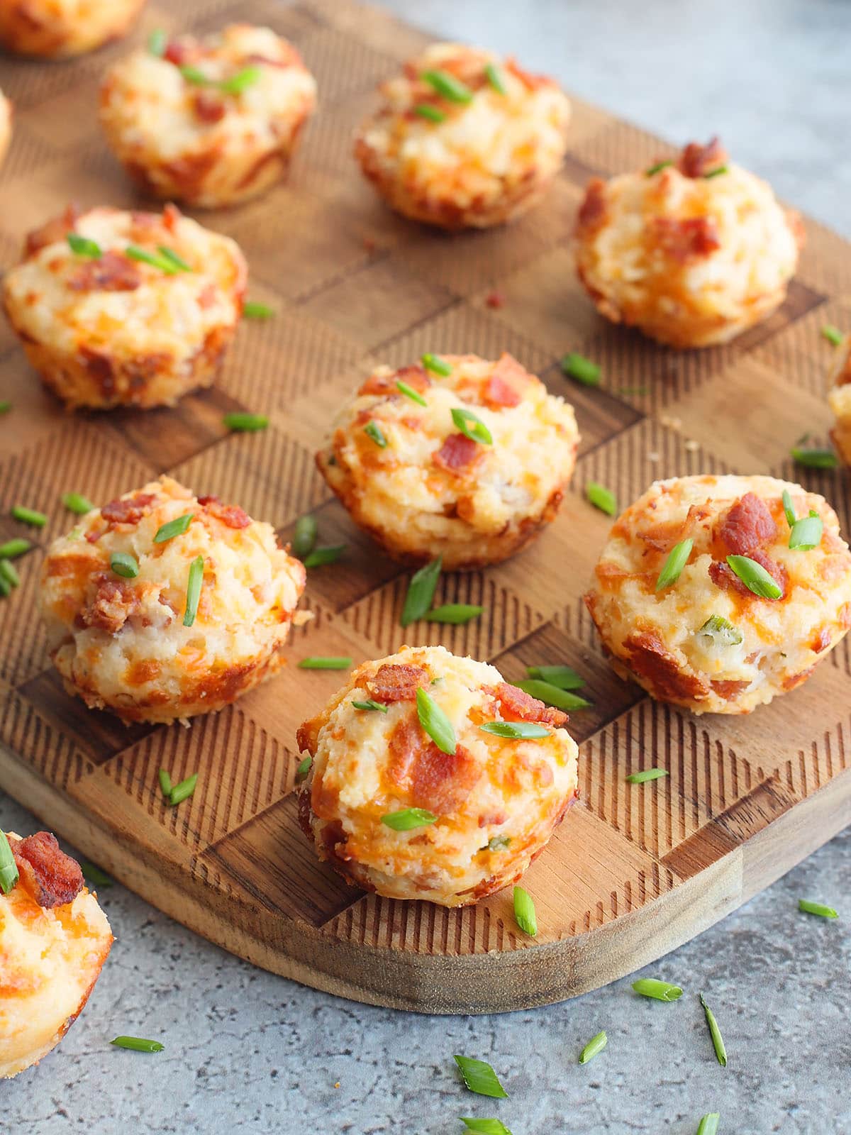 Bacon and cheese muffins garnished with fresh chives on a wooden cutting board.