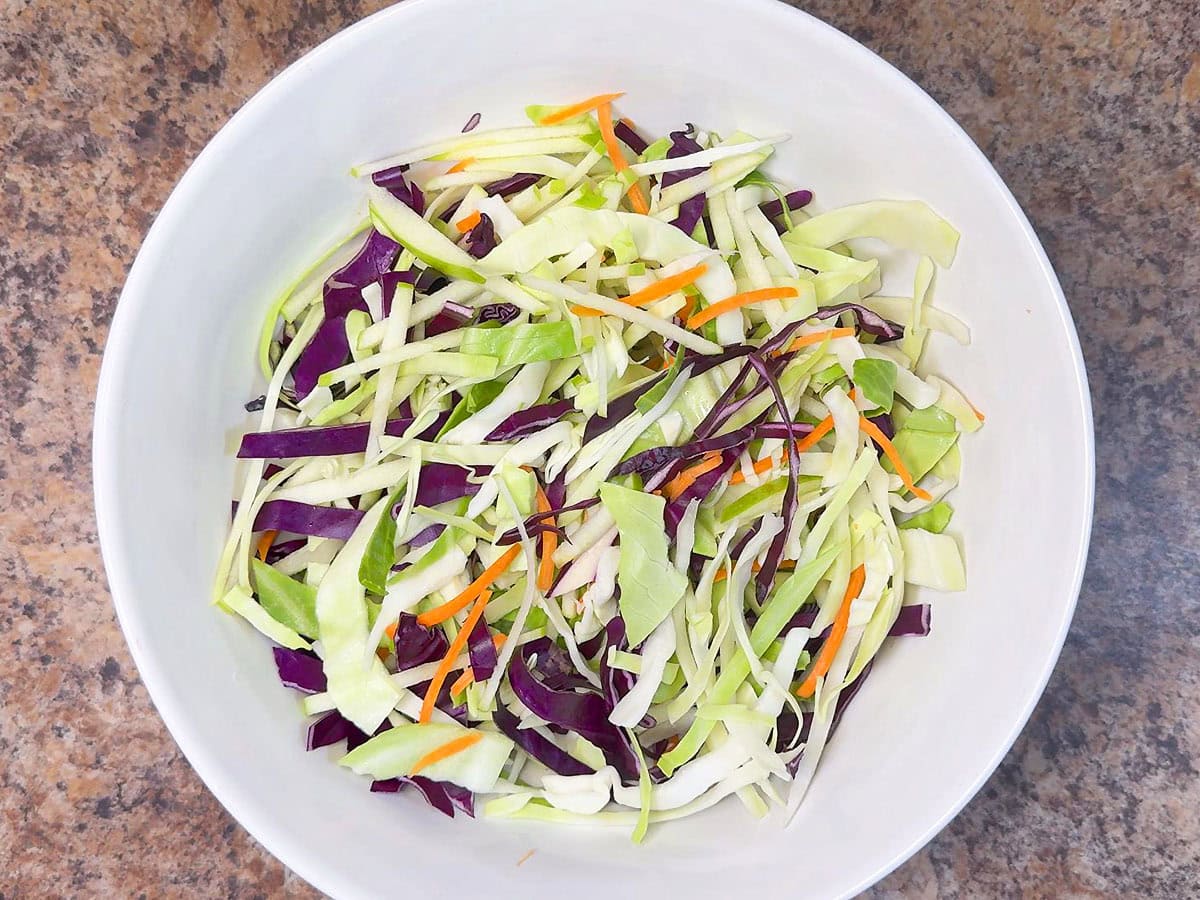 Shredded cabbage, carrots, and apples combined in a mixing bowl.