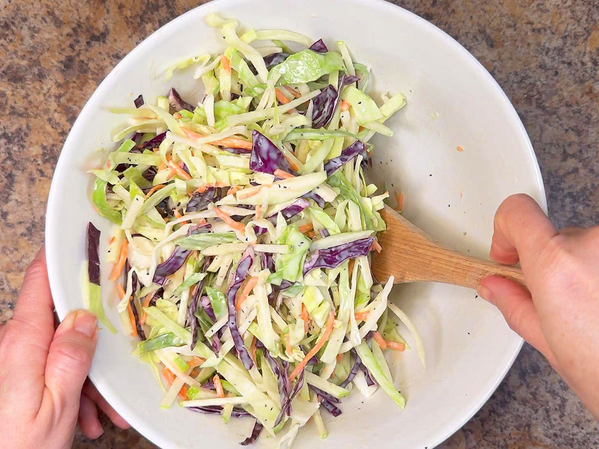 Stirring the dressing into the slaw until everything is evenly coated.