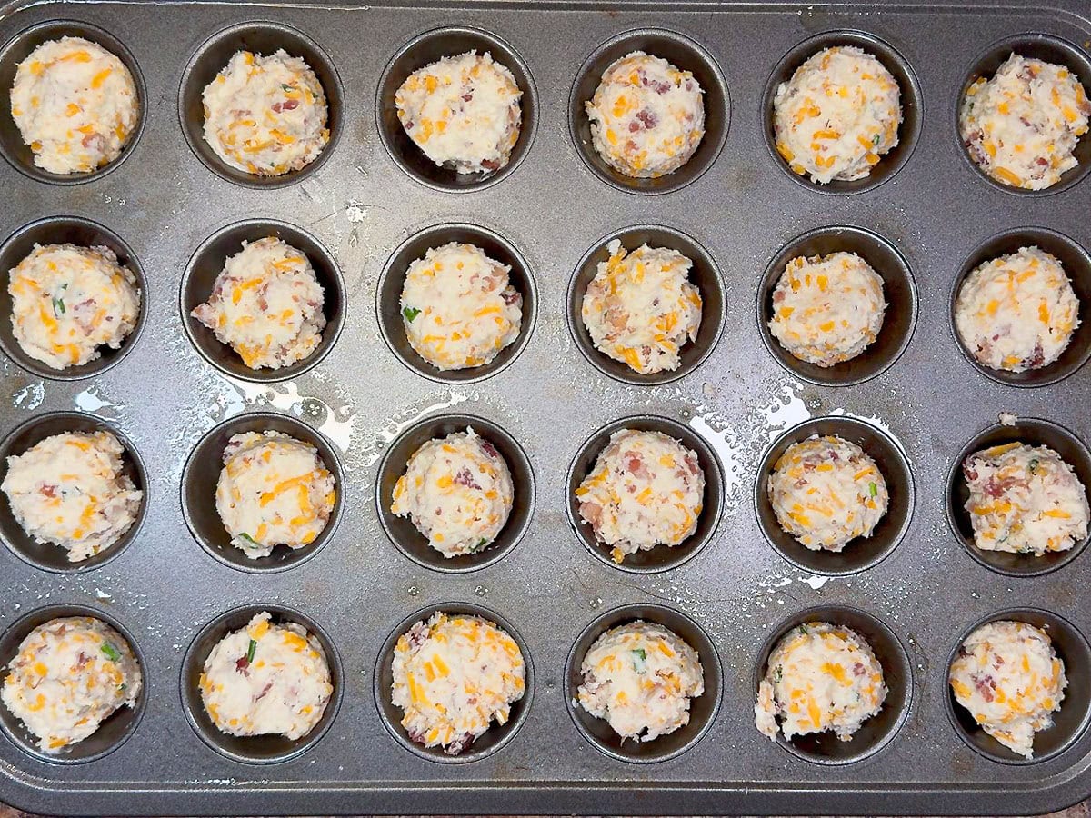 Muffin dough measured out into a greased mini muffin tin.