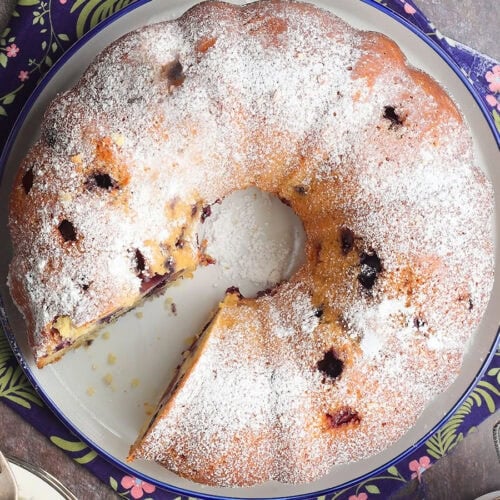 Bourbon blueberry pound cake garnished with powdered sugar on a serving plate with a slice removed.