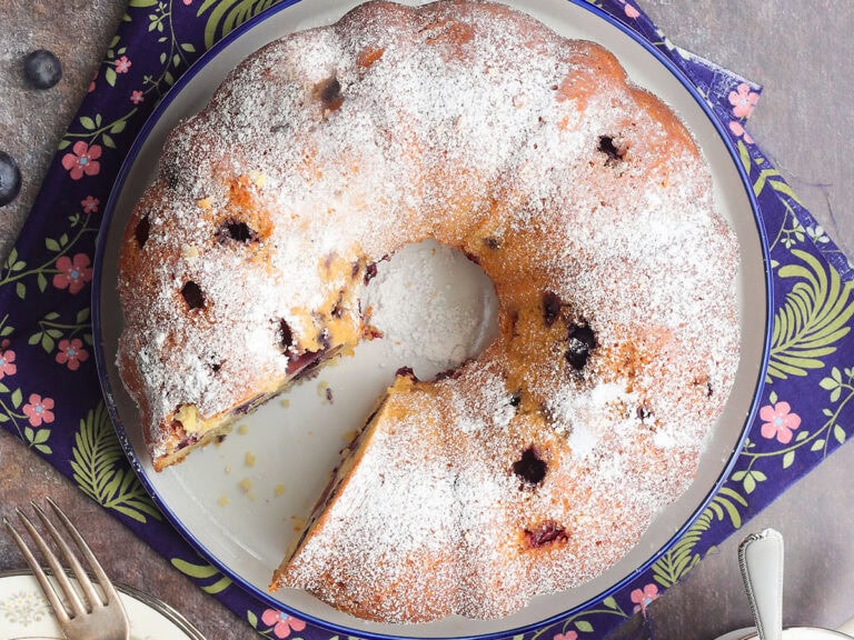 Bourbon blueberry pound cake garnished with powdered sugar on a serving plate with a slice removed.