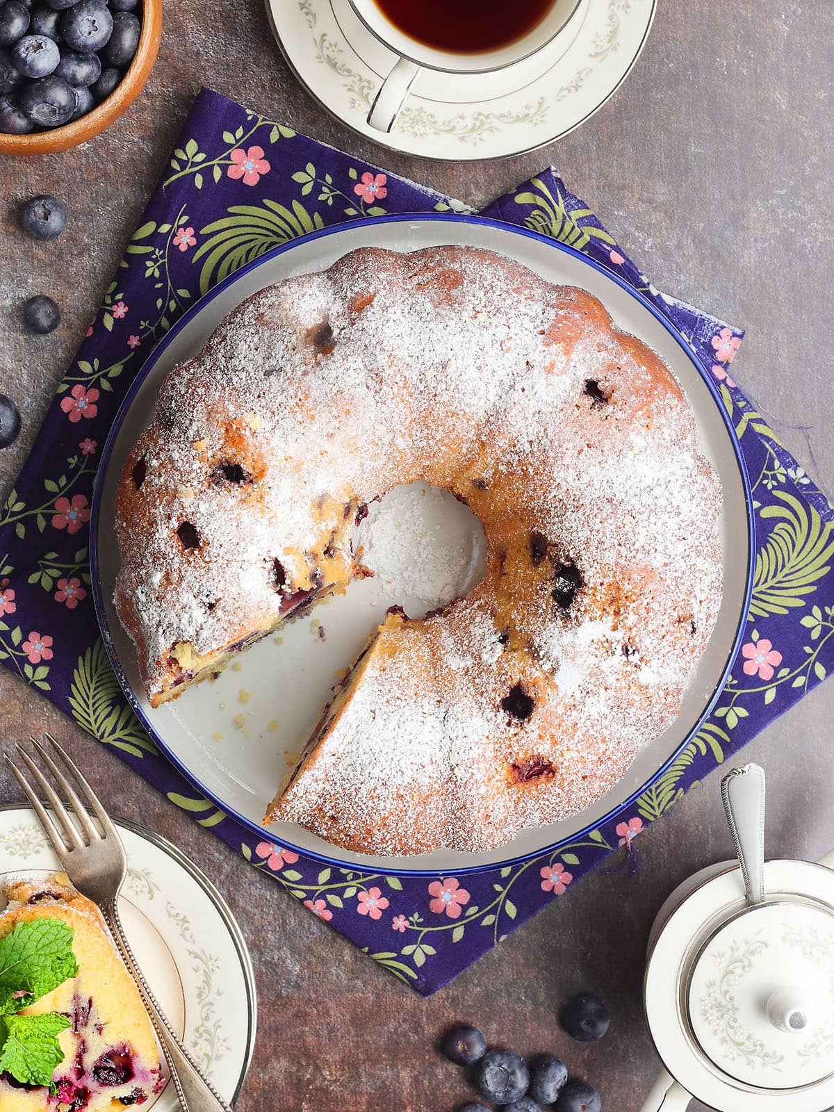 Bourbon blueberry pound cake garnished with powdered sugar on a serving plate with a slice removed.
