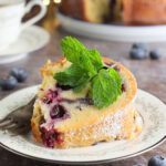 Slice of bourbon blueberry pound cake garnished with a sprig of fresh mint on a plate with a fork.