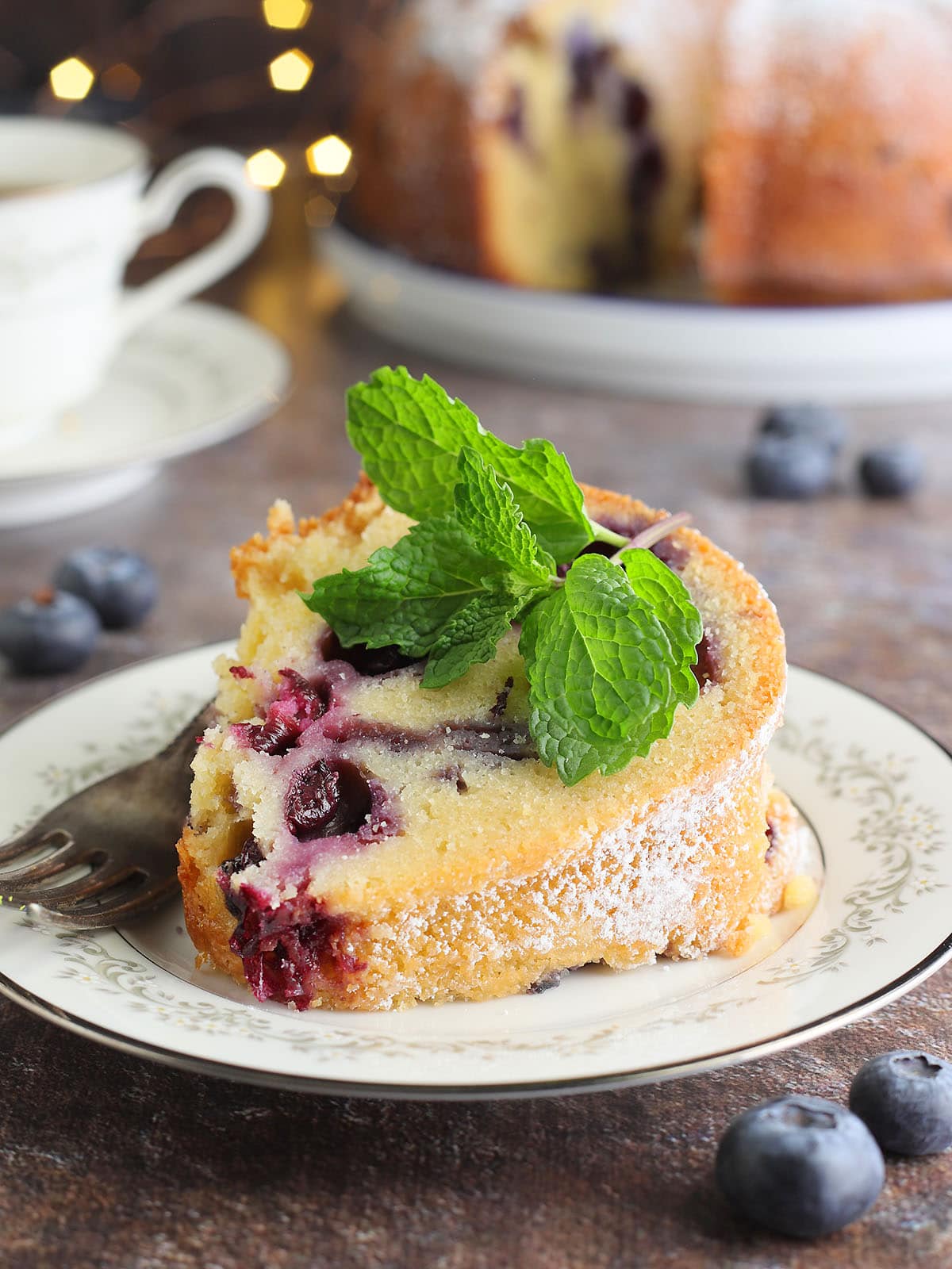 Slice of bourbon blueberry pound cake garnished with a sprig of fresh mint on a plate with a fork.