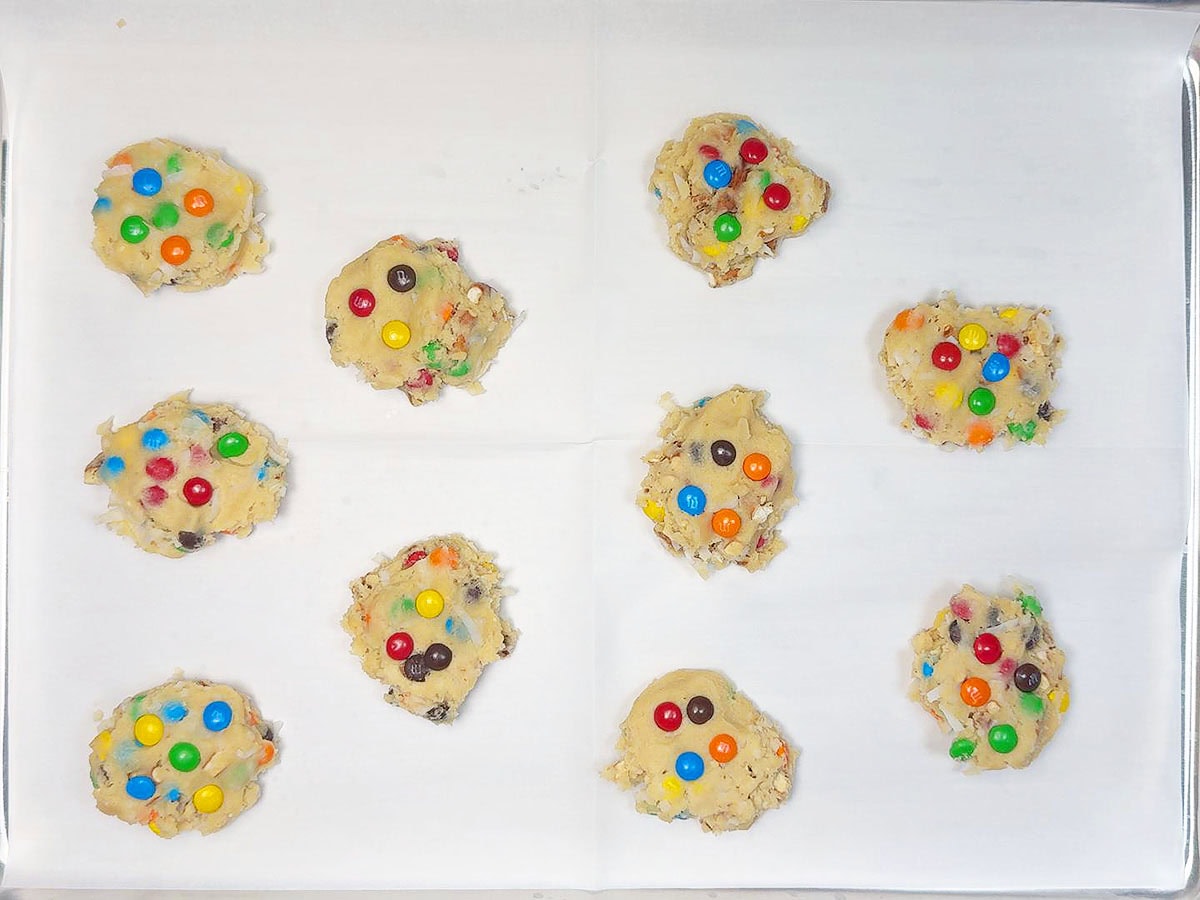 Loaded cookie dough measured out onto a parchment paper lined baking sheet.