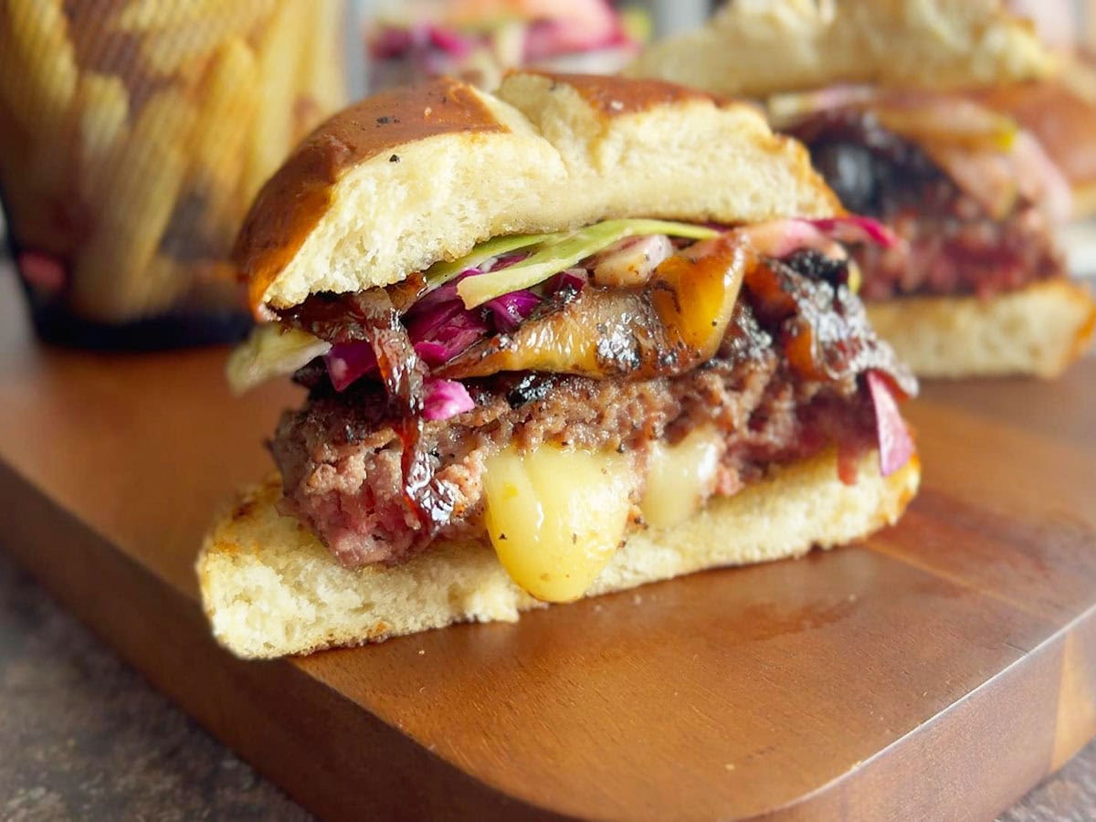 Burger that has rested for five minutes cut in half on a wooden cutting board.