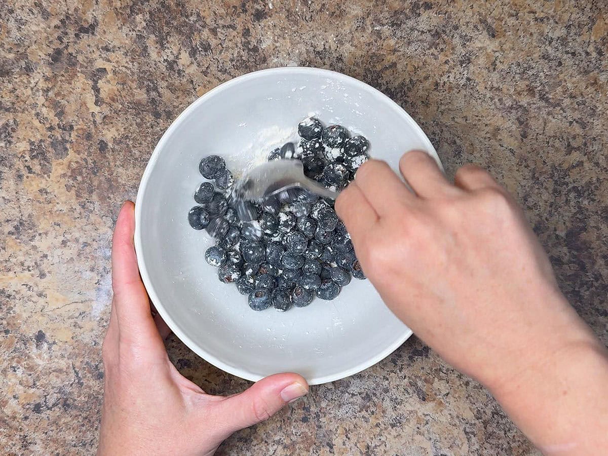 Tossing the blueberries with flour in a small bowl.