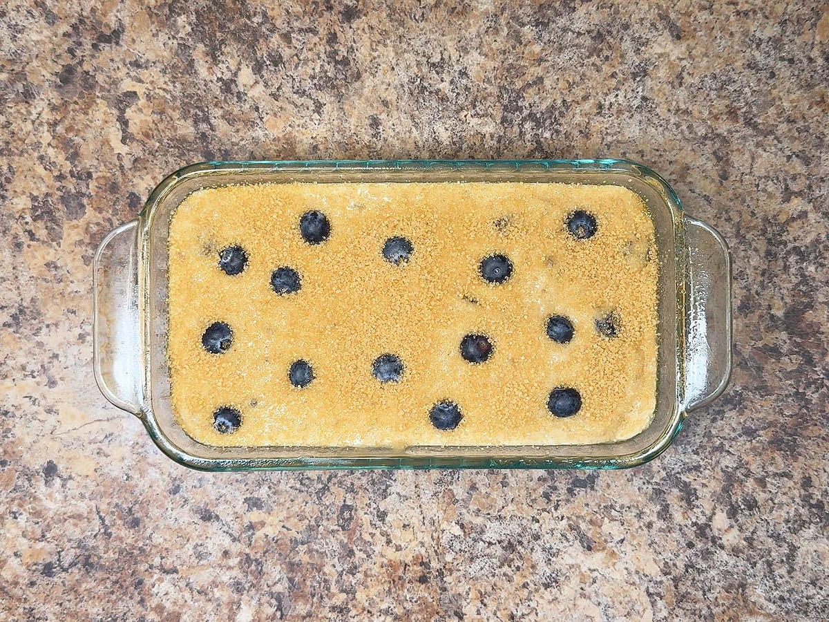Blueberry banana bread batter poured into a glass loaf pan and sprinkled with raw sugar.