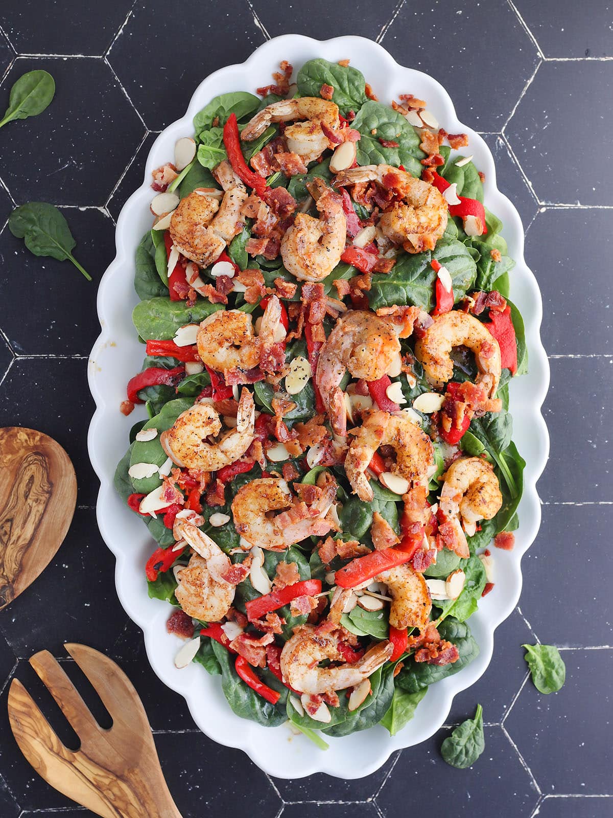 Grilled shrimp salad garnished with sliced almonds, roasted red bell peppers, and crumbled bacon on a serving platter.