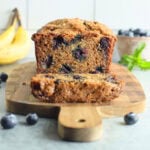 Banana bread with one slice cut away on a wooden cutting board.