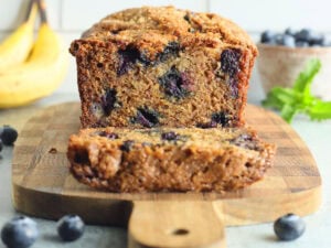 Banana bread with one slice cut away on a wooden cutting board.