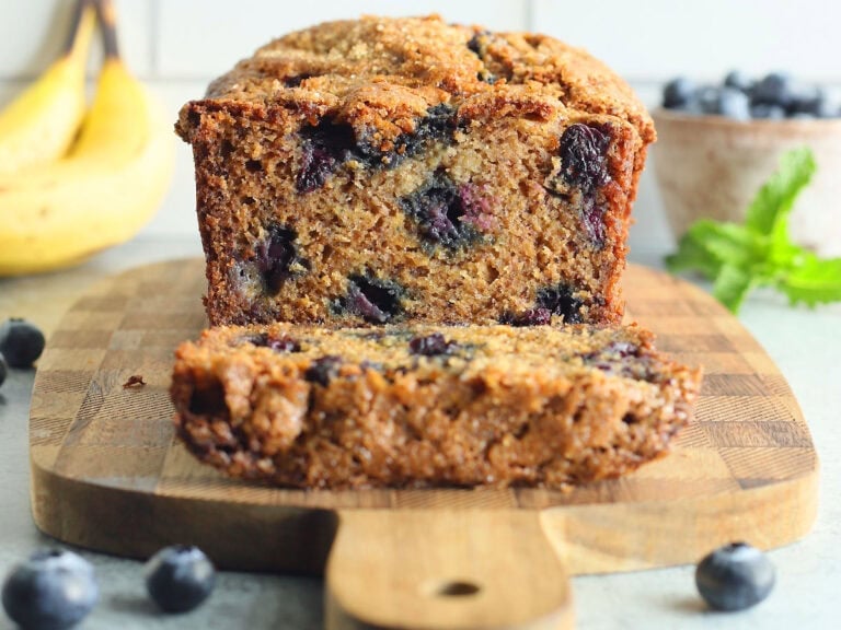 Banana bread with one slice cut away on a wooden cutting board.