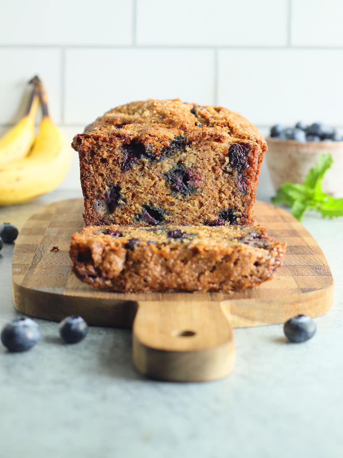 Banana bread with one slice cut away on a wooden cutting board.