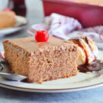 Slice of chocolate coca cola cake garnished with a cherry and a scoop of vanilla ice cream with chocolate syrup.