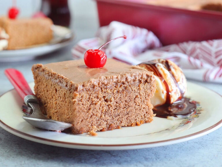 Slice of chocolate coca cola cake garnished with a cherry and a scoop of vanilla ice cream with chocolate syrup.