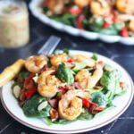 Plated grilled shrimp salad with a fork on the side, a jar of hot bacon dressing and platter of full salad in the background.