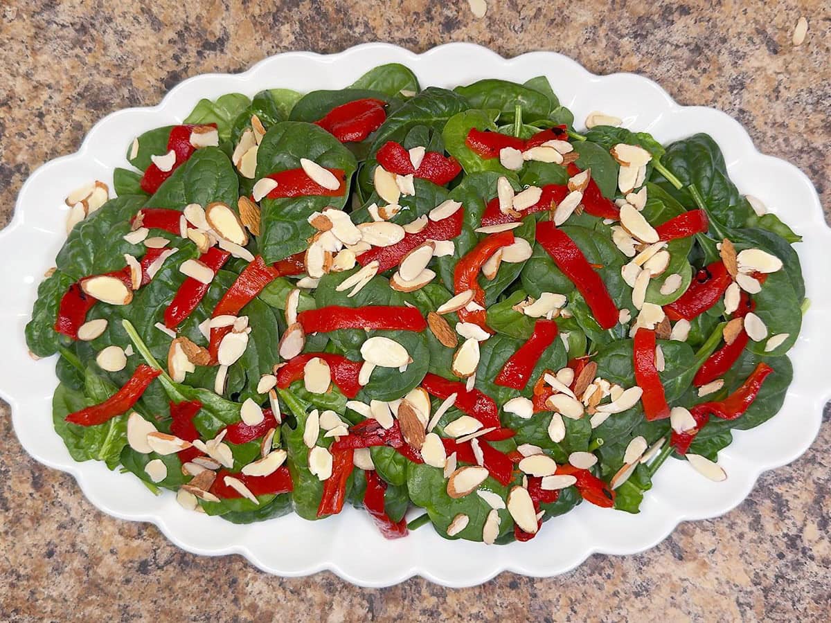 Platter topped with baby spinach, red bell pepper strips, and sliced almonds.