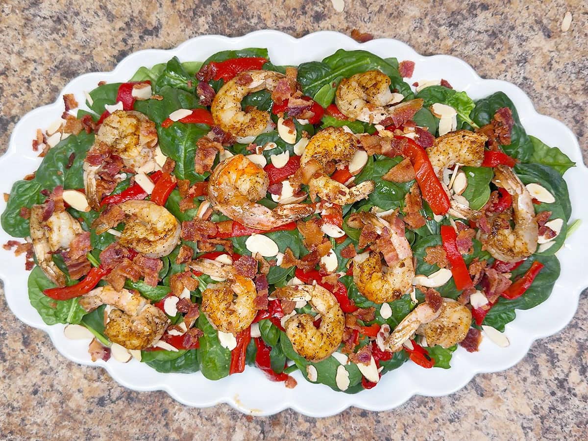 Salad on a platter topped with crumbled cooked bacon and grilled shrimp.