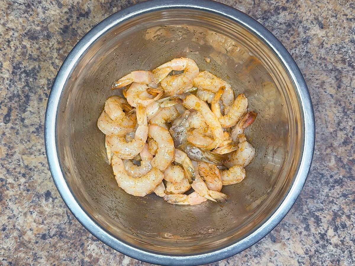 Raw shrimp seasoned with Cajun seasoning in a large mixing bowl.